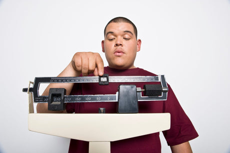 young man weighs himself on a scale to illustrate How Overweight To Get Bariatric Surgery as well as reasons for gaining weight, and How Overweight Do You Have To Be To Get Gastric Bypass