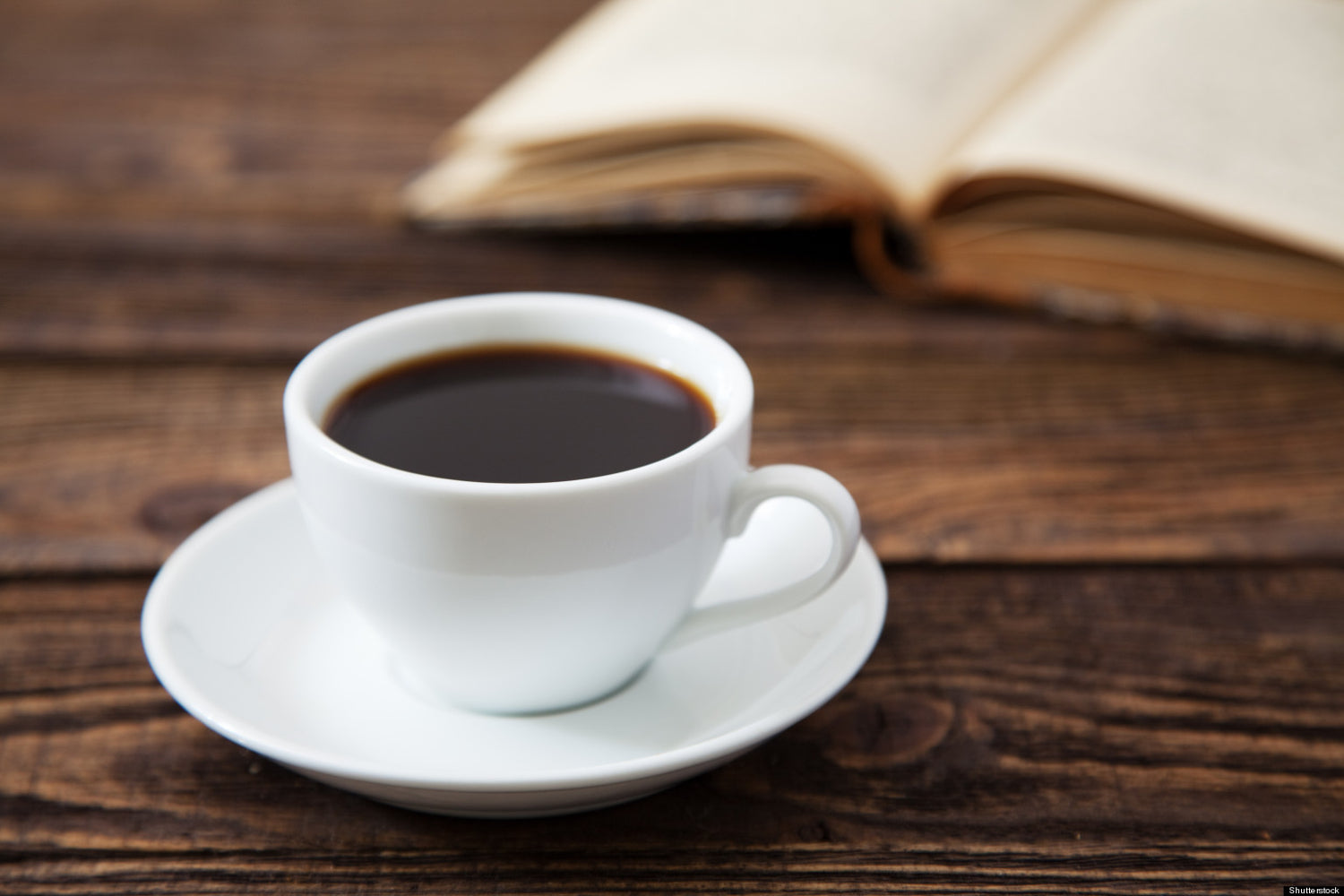 A mug of coffee next to a book on a wood table to help illustrate caffeine after gastric sleeve