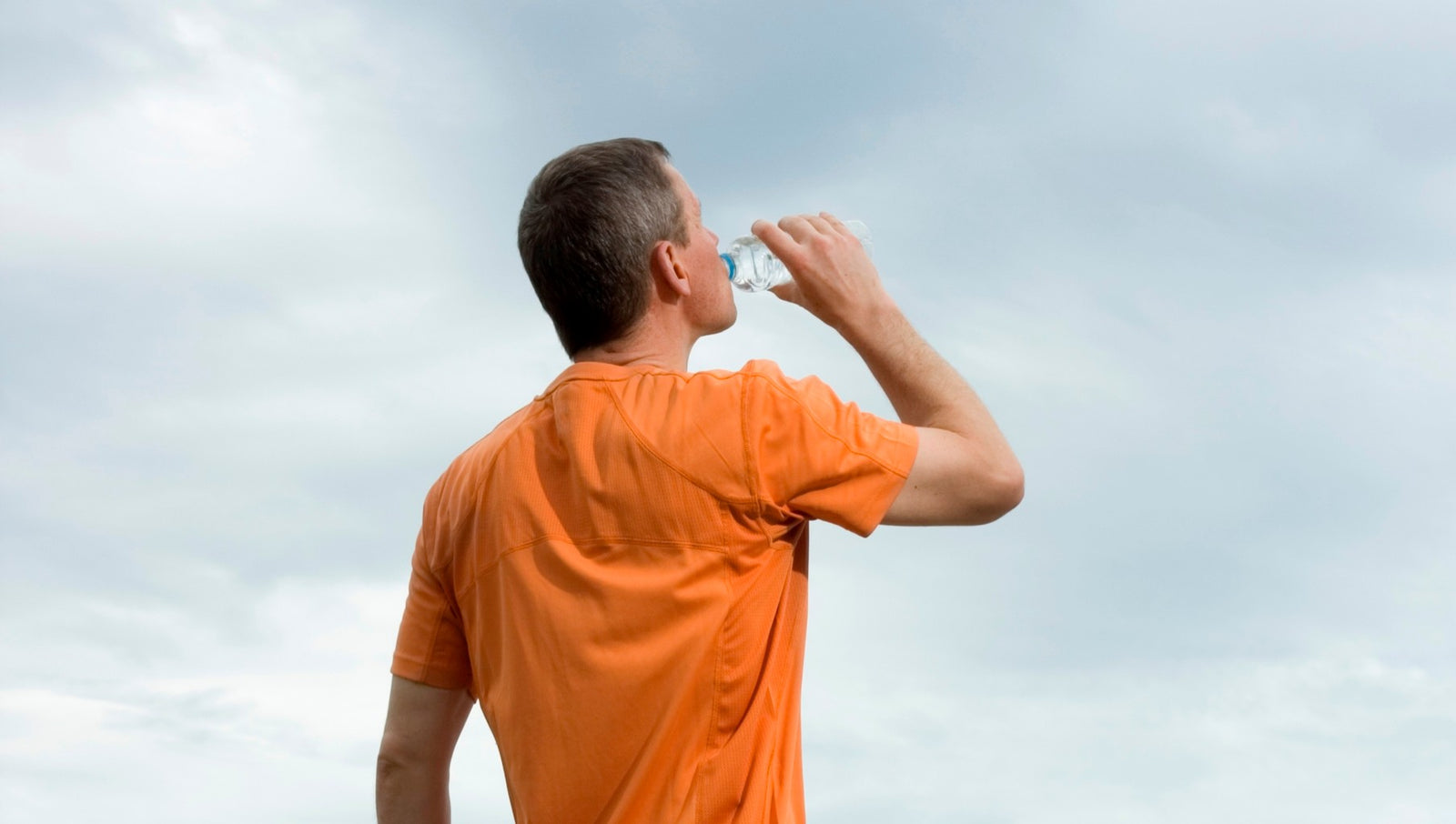 Man in orange shoirt drinking water from a bottle
