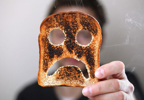 Person holding up piece of toast with unhappy face cut out.