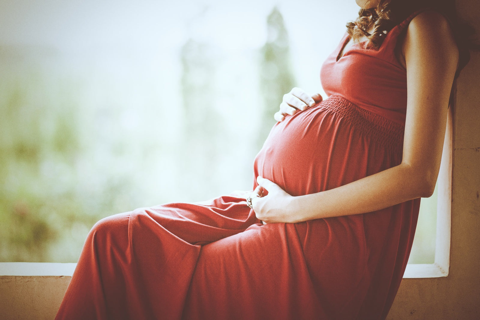 Woman in a red dress holding her pregnant stomach to illustrate pregnancy after gastric sleeve and pregnancy after weight loss suregry